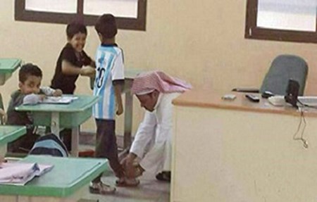صورة: معلم ينحني لربط حذاء طالب