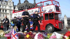 Armed police officers pass tributes in Parliament Square following a recent attack in Westminster, London