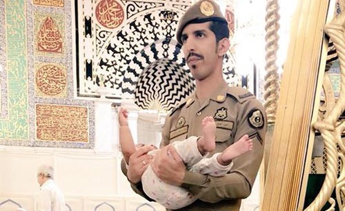 شاهد.. صورة لعسكري سعودي يحمل طفلا بالمسجد النبوي كي يتمكن والده من الصلاة